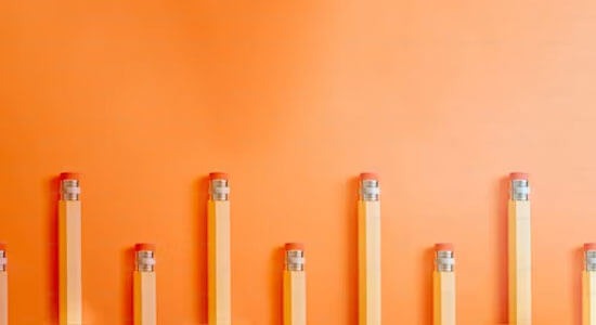 A row of pencils of different lengths, arranged in ascending order on an orange background.